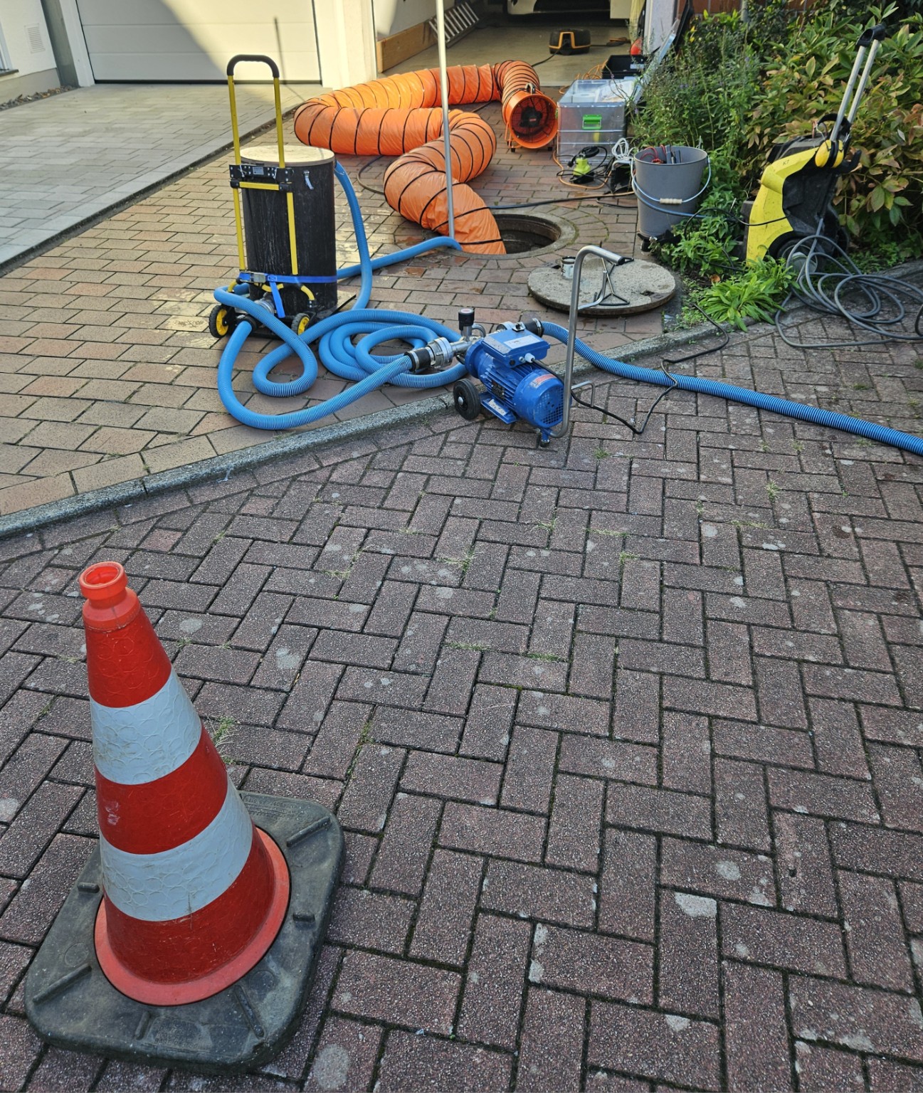 Pumpen und blaue Saugschläuche zum Schlammabsaugen neben einem geöffneten Zisternenschacht mit orangefarbenem Lüftungsschlauch